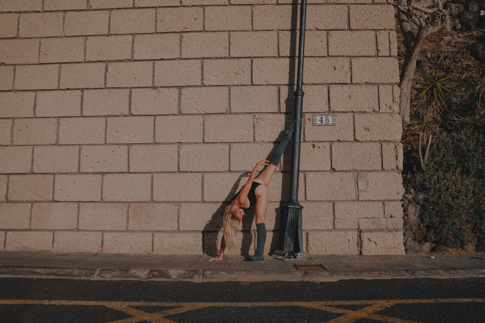 woman in black jacket and black pants holding black rifle leaning on brown brick wall