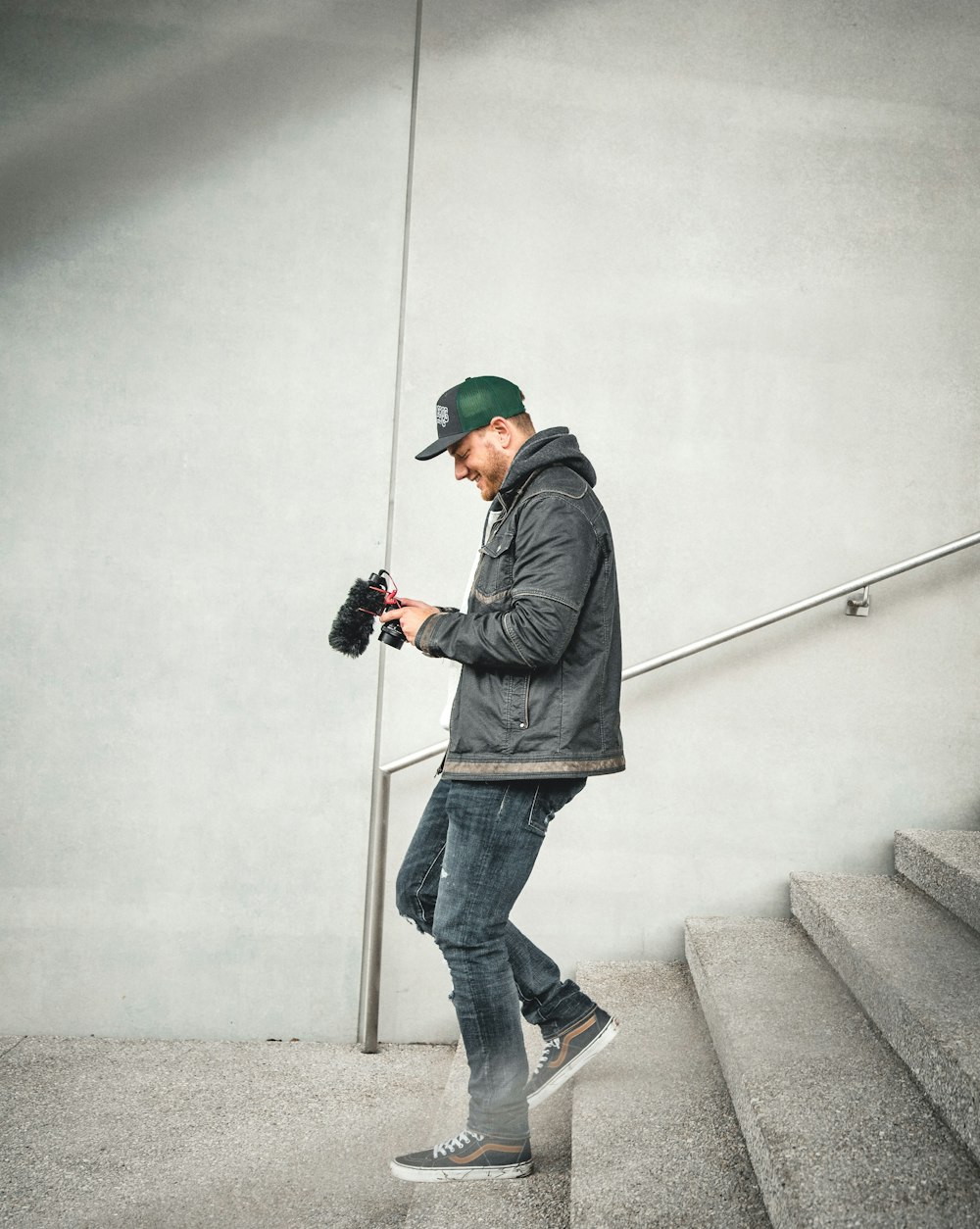 man in black jacket and blue denim jeans using black dslr camera