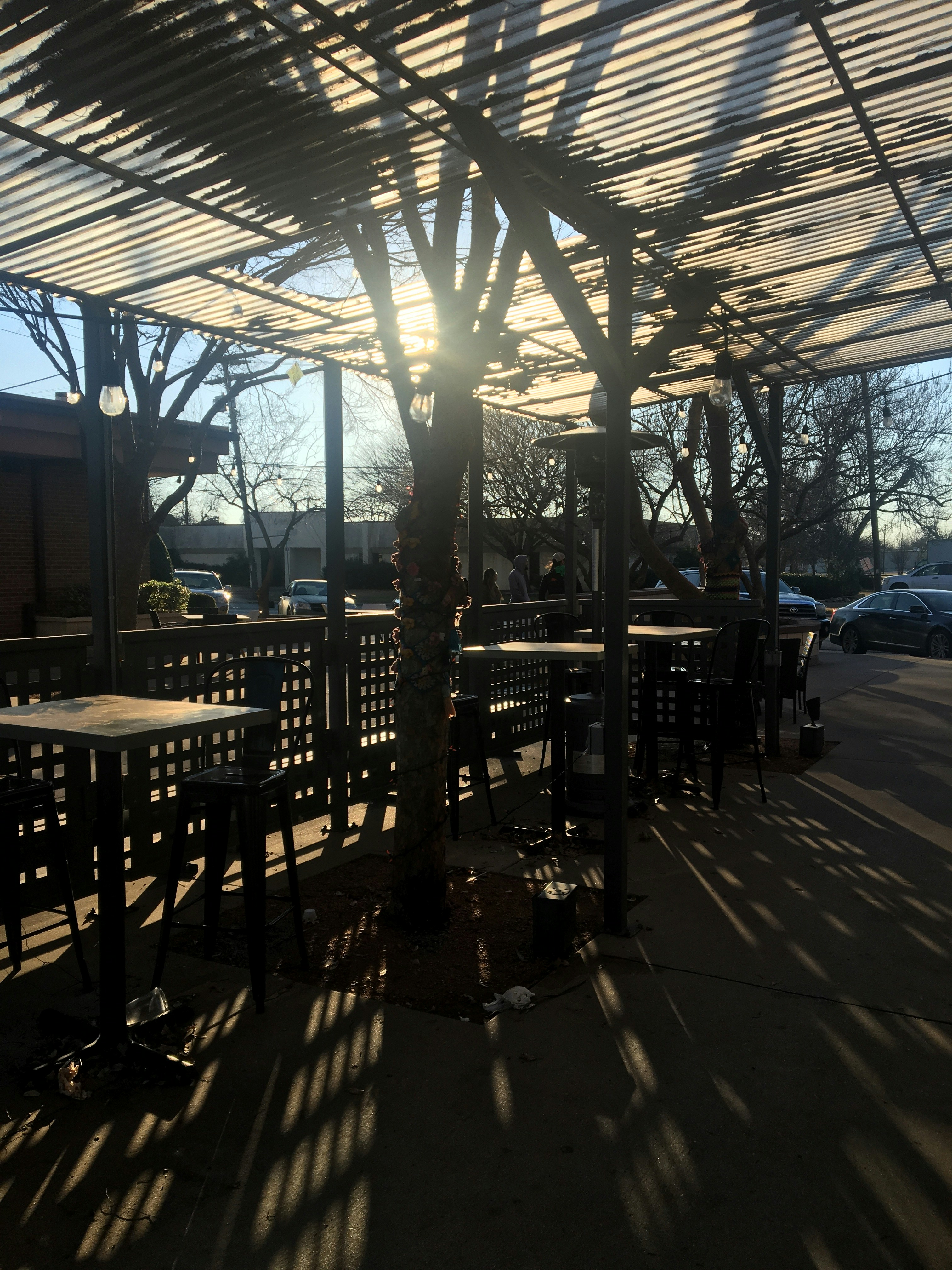 Large aluminum patio cover with exposed timber beams over a stone patio, afternoon light filtering through