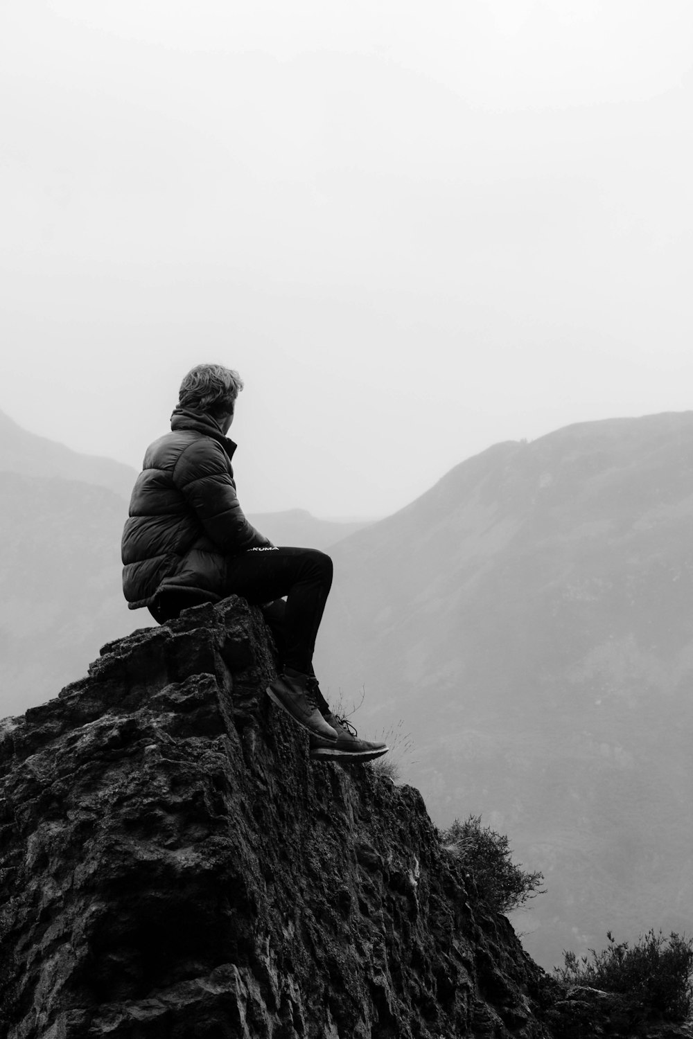 man in black jacket sitting on rock formation during daytime