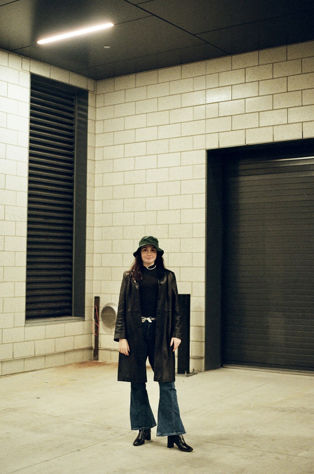 woman in brown coat standing near gray wall