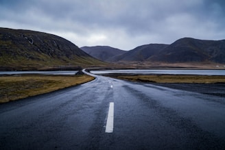 gray concrete road near green mountain under white clouds during daytime