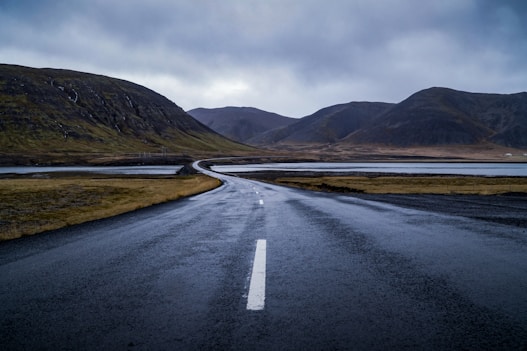 gray concrete road near green mountain under white clouds during daytime
