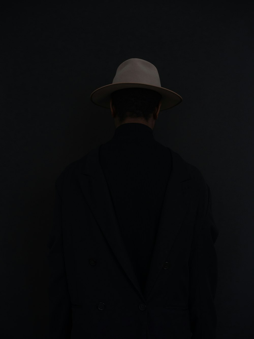 Homme en costume noir portant un chapeau fedora blanc