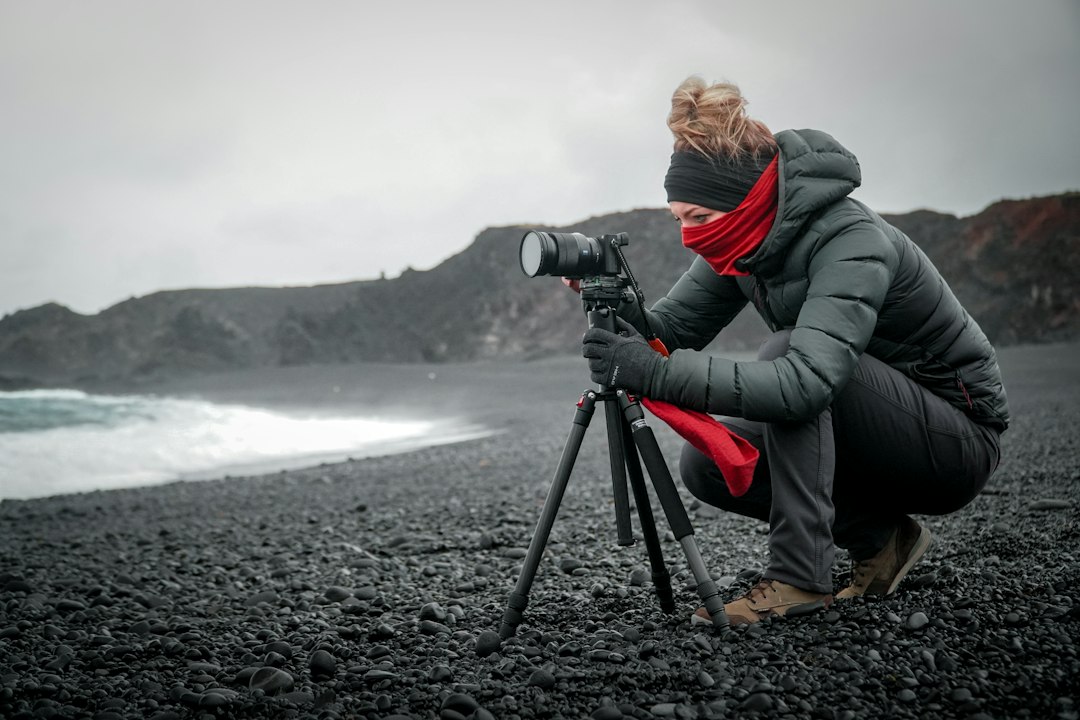 person in gray jacket and gray pants holding black dslr camera, Gloves were a must on the beach during this cold October