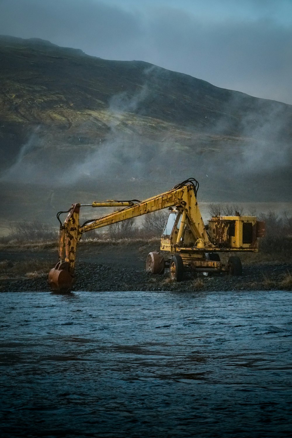 yellow excavator on water near mountain