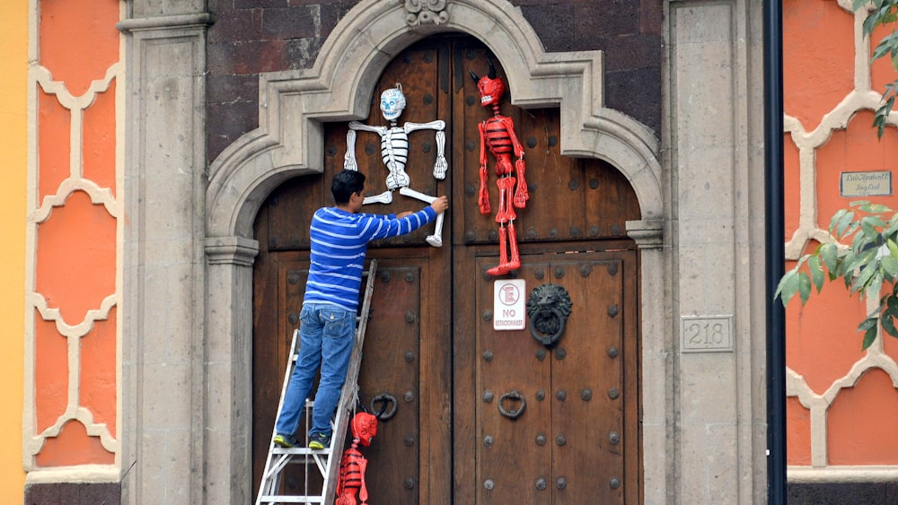 homem na camisa azul de manga comprida e calças azuis de pé ao lado da porta de madeira marrom