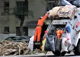 man in orange jacket and blue denim jeans standing near garbage