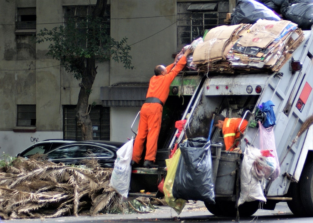 man in orange jacket and blue denim jeans standing near garbage