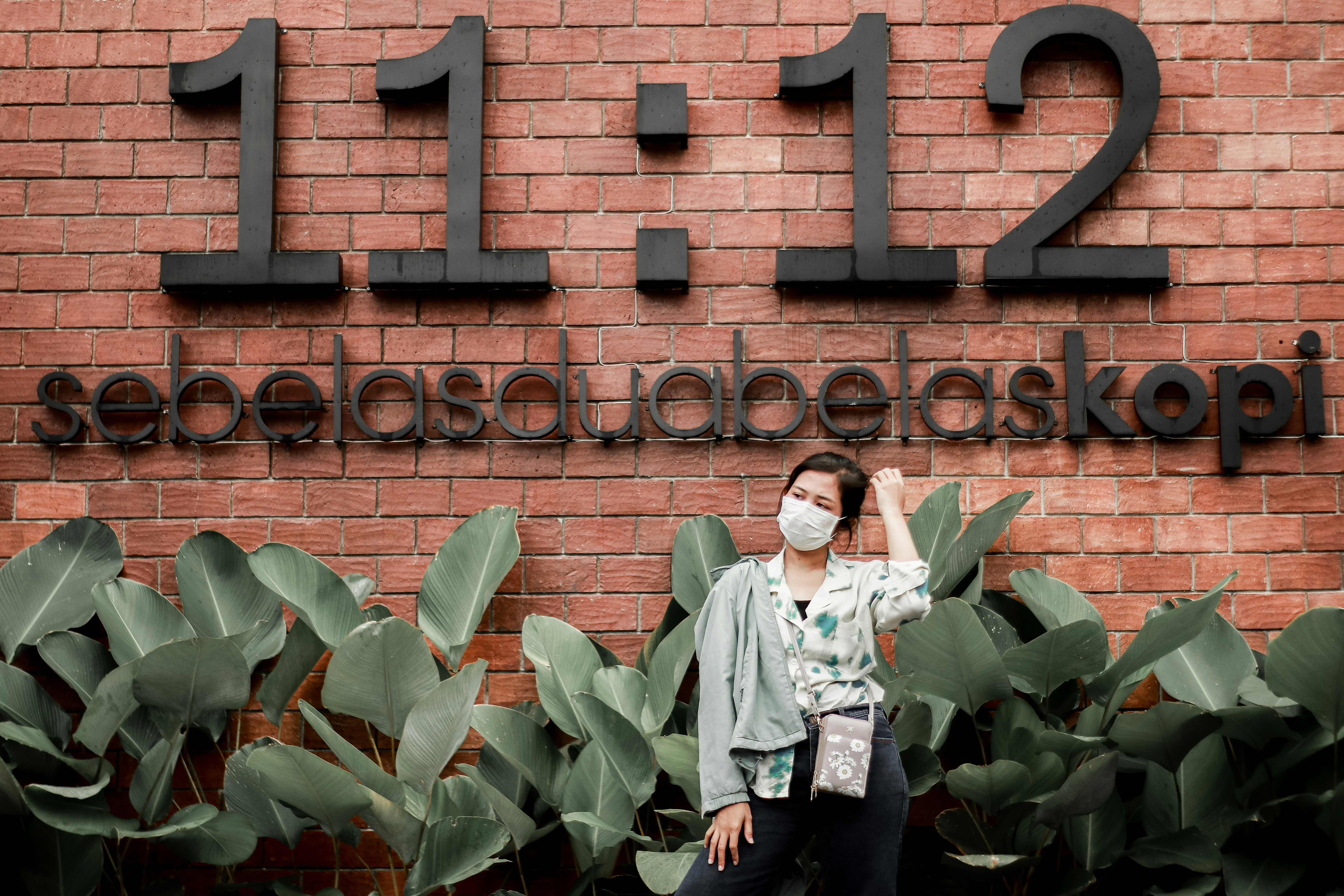 woman in white long sleeve shirt and black pants standing beside brown brick wall during daytime