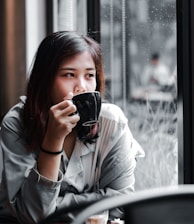 woman in white long sleeve shirt holding black ceramic mug