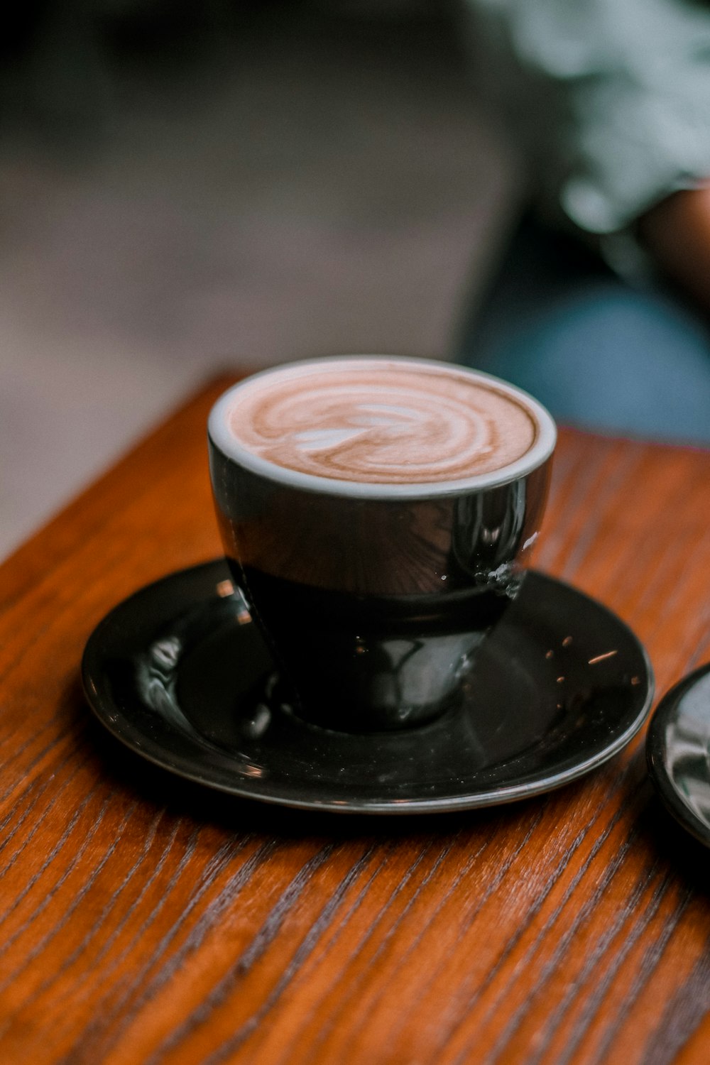 schwarze Keramiktasse mit Untertasse auf braunem Holztisch