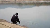 A consultant in a blue shirt examining water quality by a calm lake.