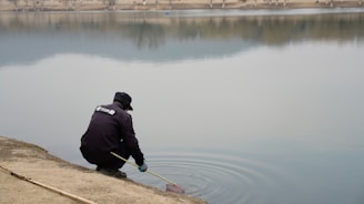 A consultant in a blue shirt examining water quality by a calm lake.