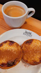 A stack of golden Portuguese bolachas on a minimalist wooden board with a cup of coffee.