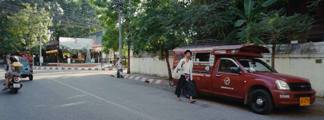 man in white dress shirt standing beside red car during daytime