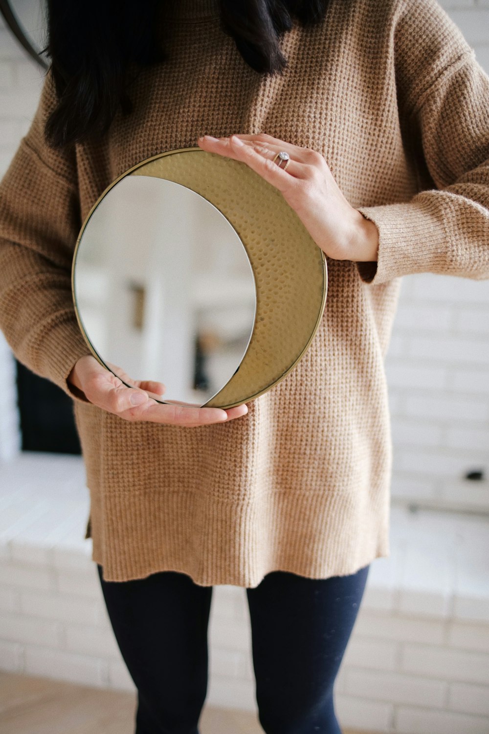 woman in beige long sleeve shirt and black skirt holding round mirror