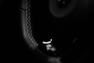 Close-up view of a car's steering wheel, showcasing intricate stitching along the edge. The image features a black and white color scheme, emphasizing the texture and craftsmanship.