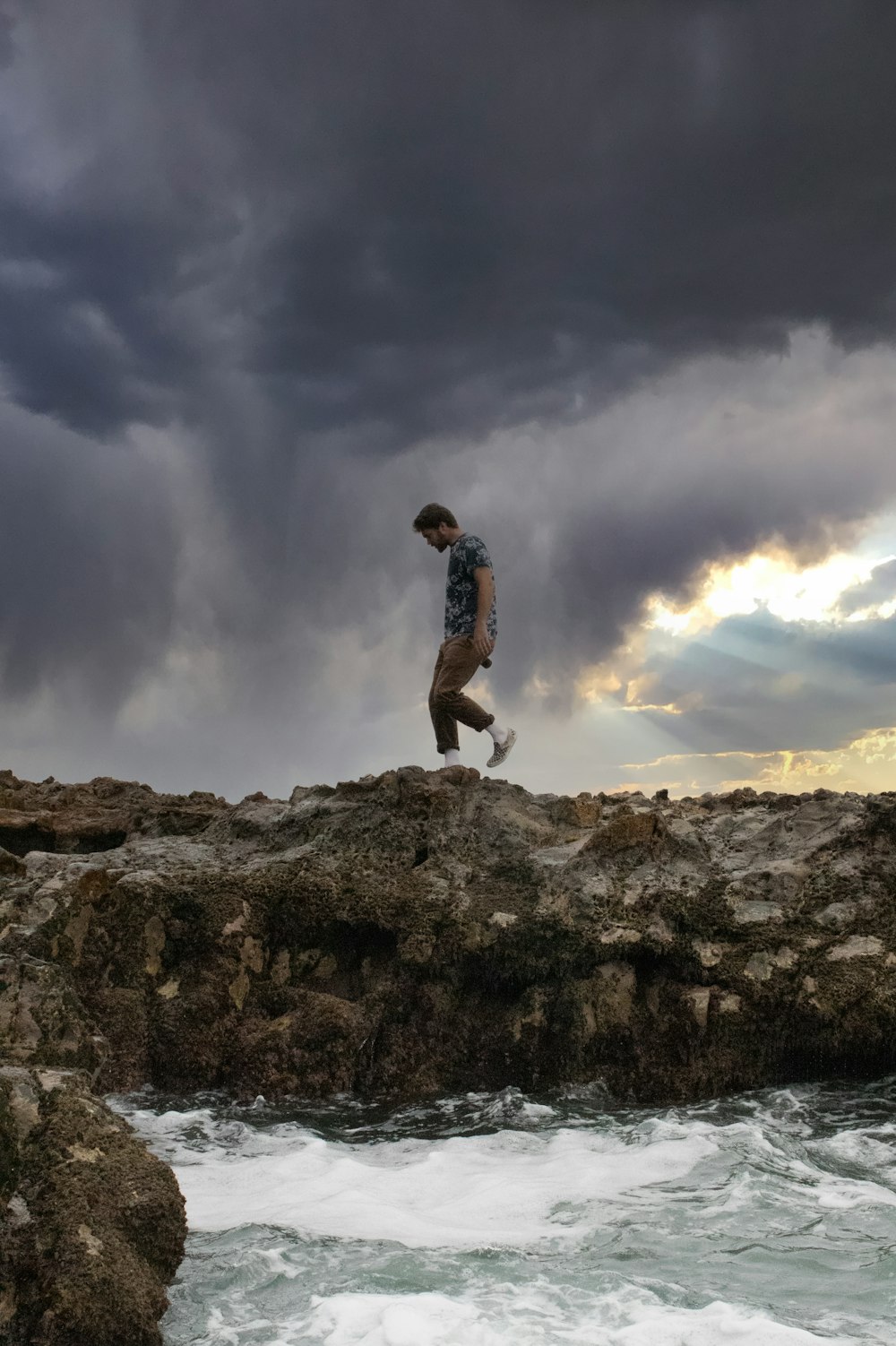 man in black tank top and black shorts standing on rock formation under cloudy sky during