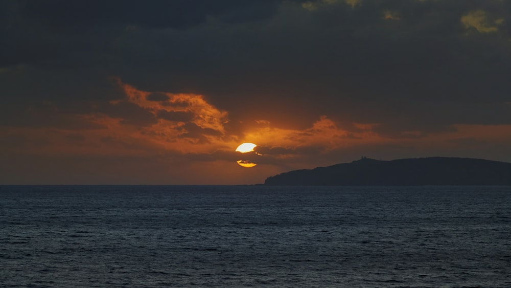 silhouette of mountain near body of water during sunset