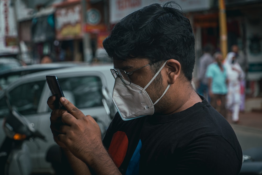 man in black long sleeve shirt wearing white face mask holding black smartphone