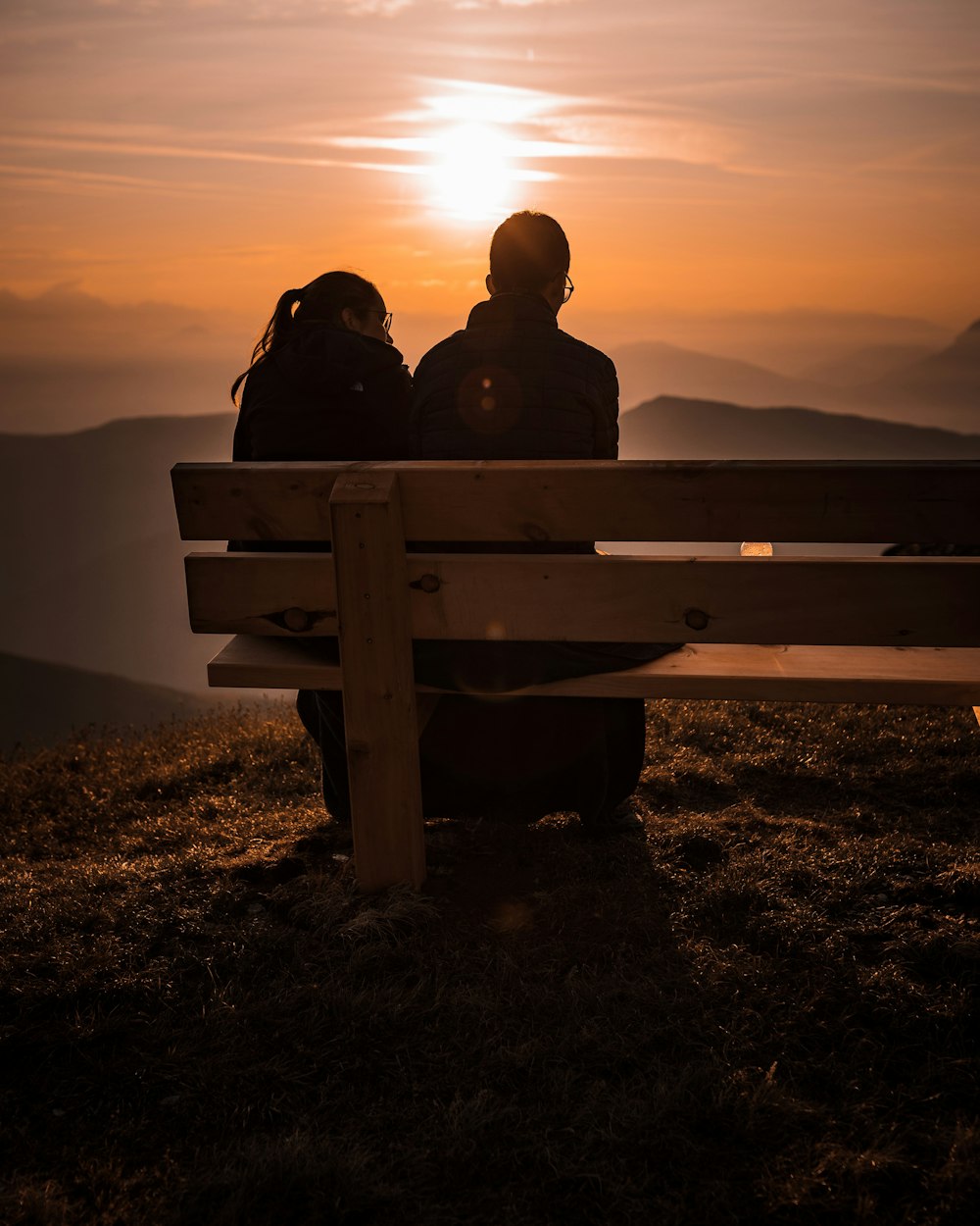 silhouette of 2 person sitting on bench during sunset