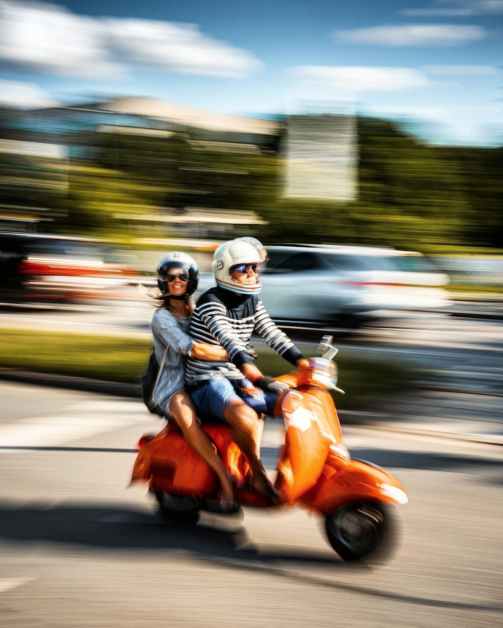 昼間の道路でオレンジ色のスクーターに乗る黒いジャケットの男