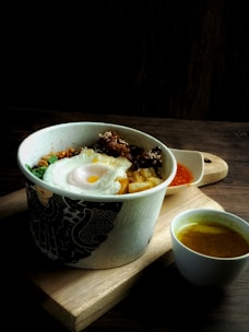 A rustic wooden board with boiled eggs, steamed veggies, and a small bowl of dipping sauce.