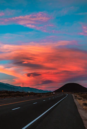 A winding road stretching into a colorful sunset sky with the RV driving along