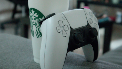 A steaming cup of coffee next to a game controller on a wooden table.
