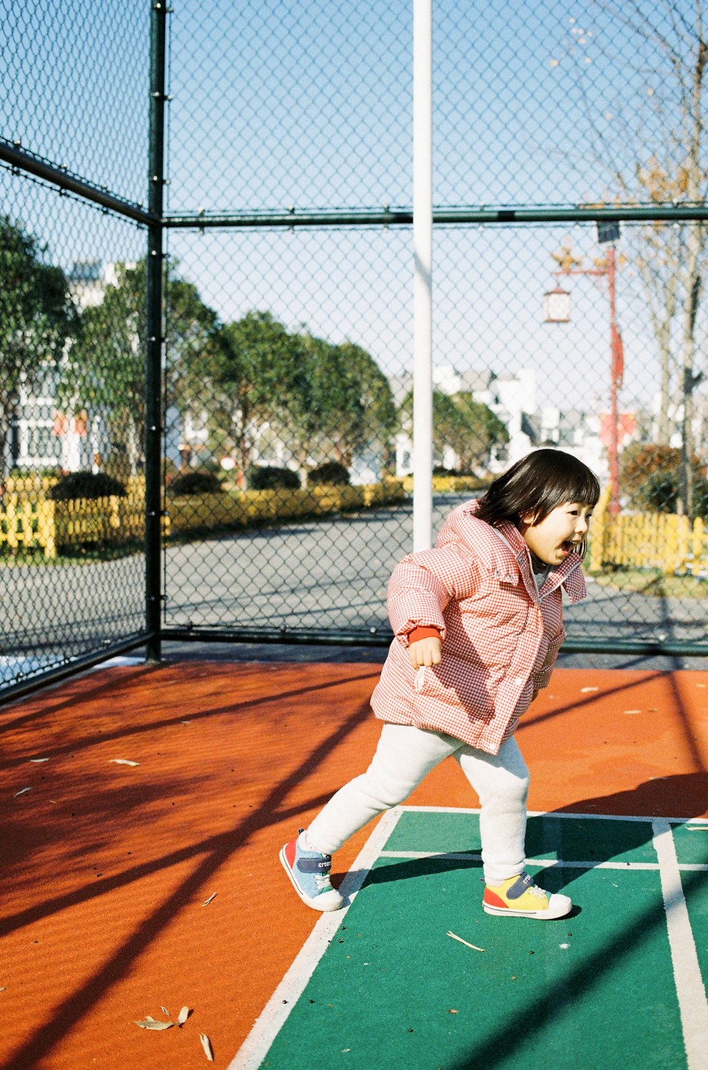 girl in pink jacket and white pants playing tennis during daytime