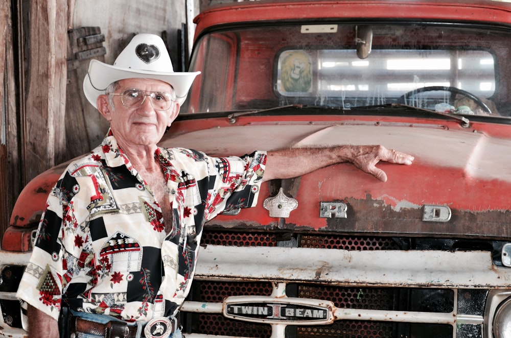 man in white cowboy hat and red and white button up shirt sitting on red car