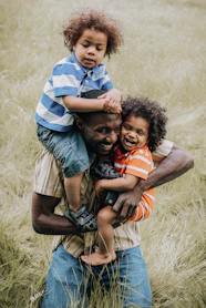 man in blue and white stripe polo shirt carrying baby in orange and black carrier
