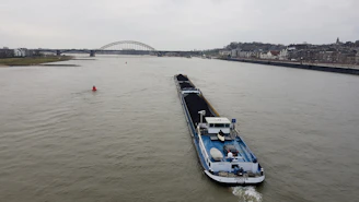 Cargo ship loaded with coal containers navigating a calm river at sunset.