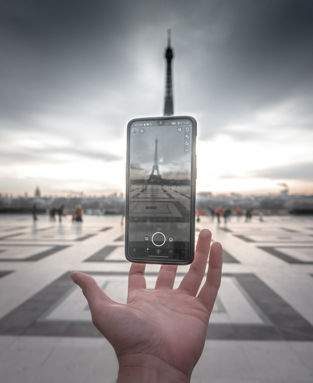 Une personne tenant un téléphone portable devant la Tour Eiffel