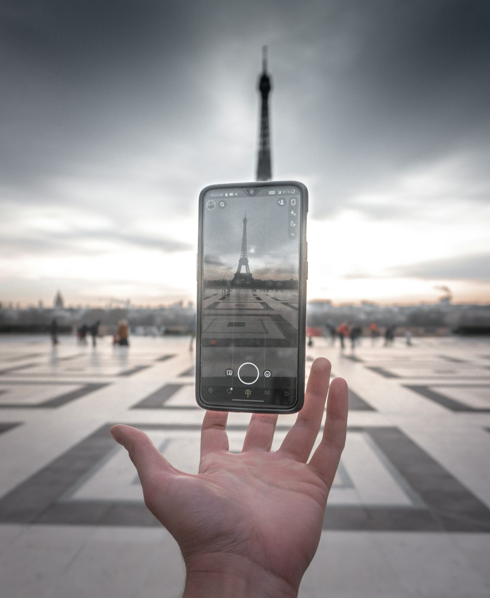 a person holding up a cell phone in front of the eiffel tower