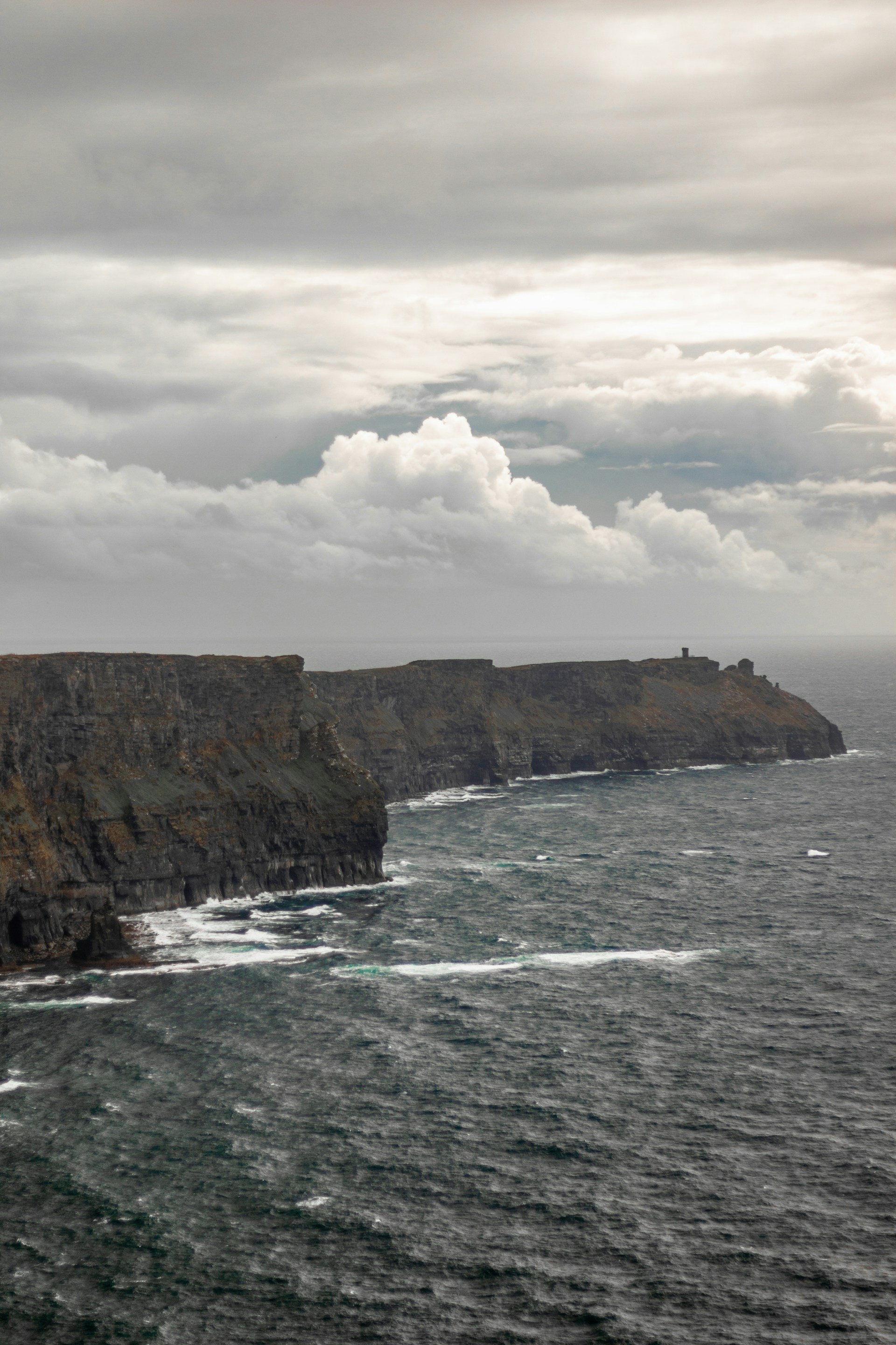 A dramatic shot of towering ocean waves crashing against rugged coastal cliffs under a moody sky.