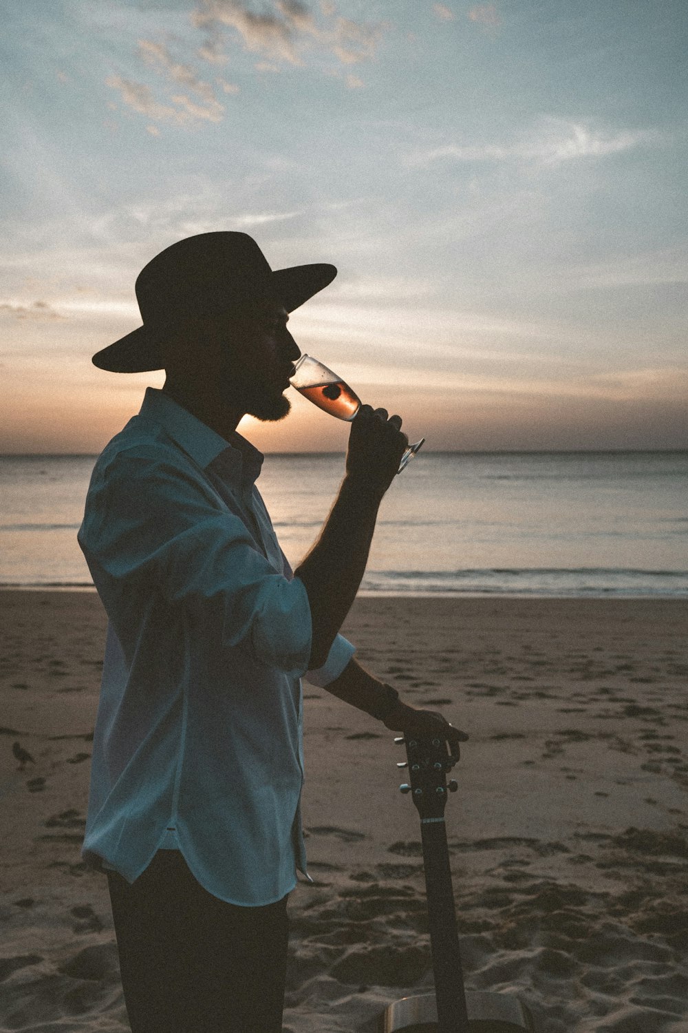 homem na camisa social branca e chapéu de cowboy preto segurando câmera dslr preta na praia durante