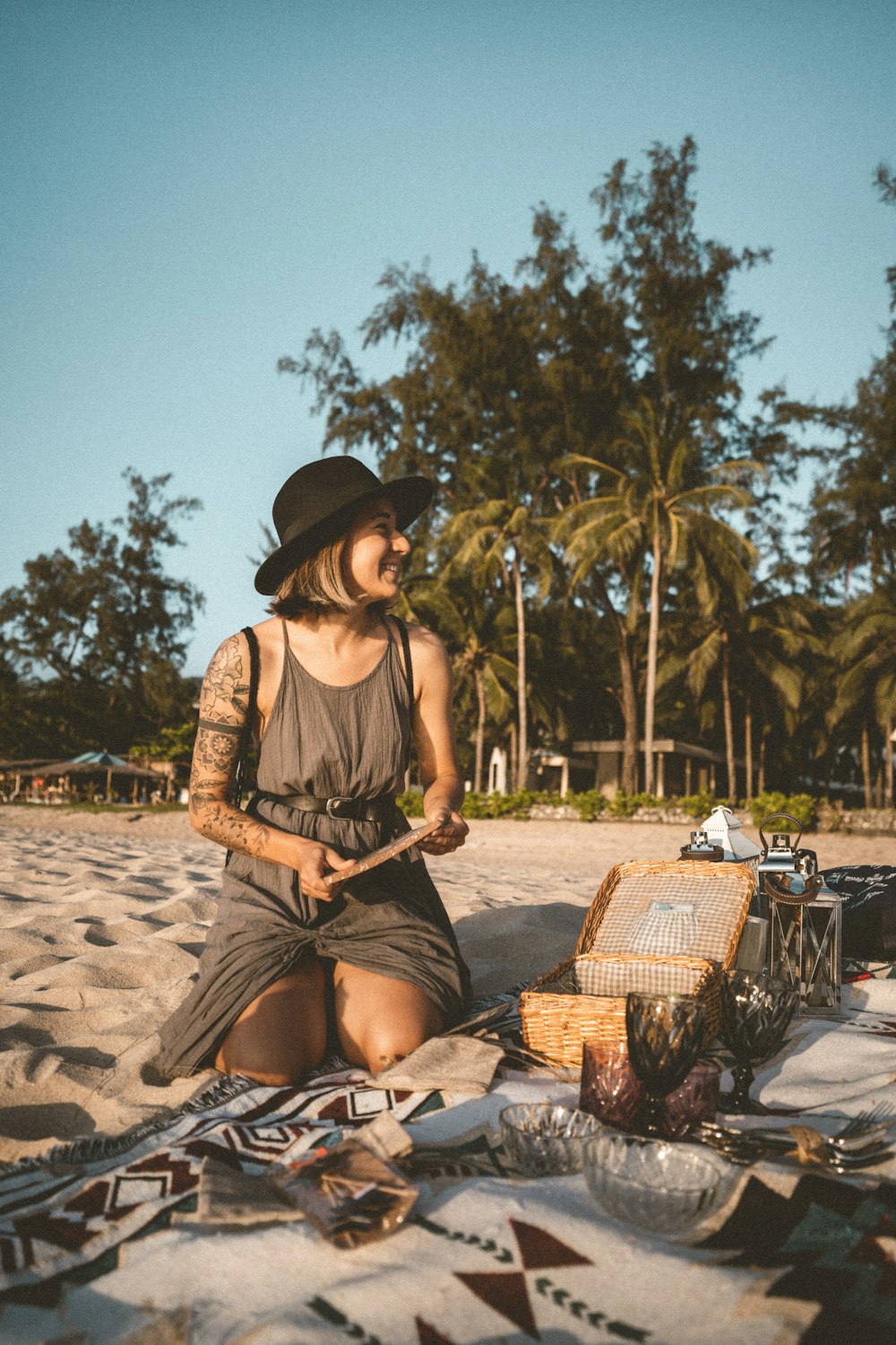 茶色のシャツと黒いスカートを着た女性が、昼間、ビーチで茶色の編まれた椅子に座っている