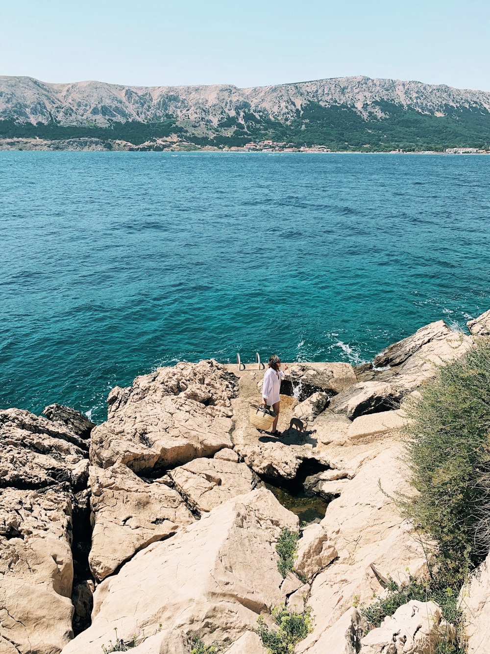 person in white shirt sitting on rock near body of water during daytime