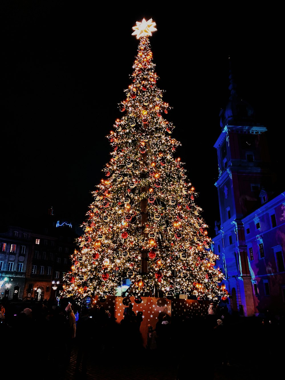 Gente caminando en la calle cerca del árbol de Navidad con luces de cadena durante la noche
