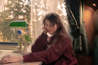 A warm, inviting portrait of Marie Fletcher sitting by a window with a notebook and pen, soft natural light highlighting her calm expression.