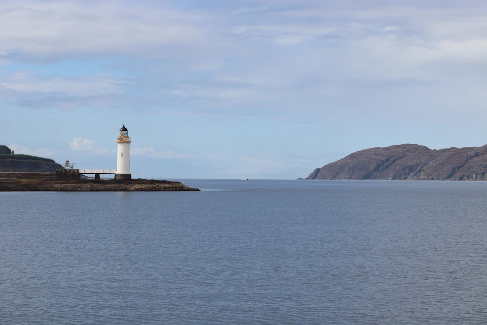 White lighthouse stands tall on rocky outcropping near shoreline, surrounded by vast ocean waters