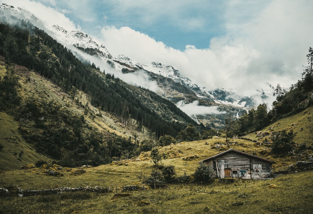 Braunes Holzhaus auf grünem Grasfeld in der Nähe des Berges unter weißen Wolken tagsüber