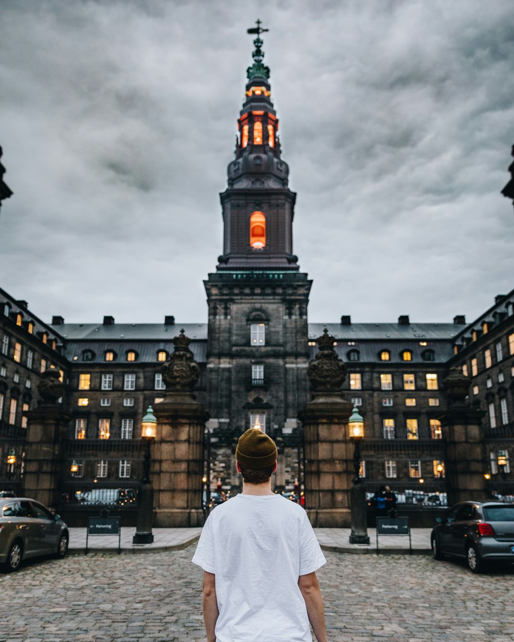 man in white shirt standing near brown concrete building during daytime