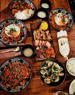 A vibrant spread of Korean dishes and beverages displayed on a wooden table with Seoul city lights softly glowing in the background.