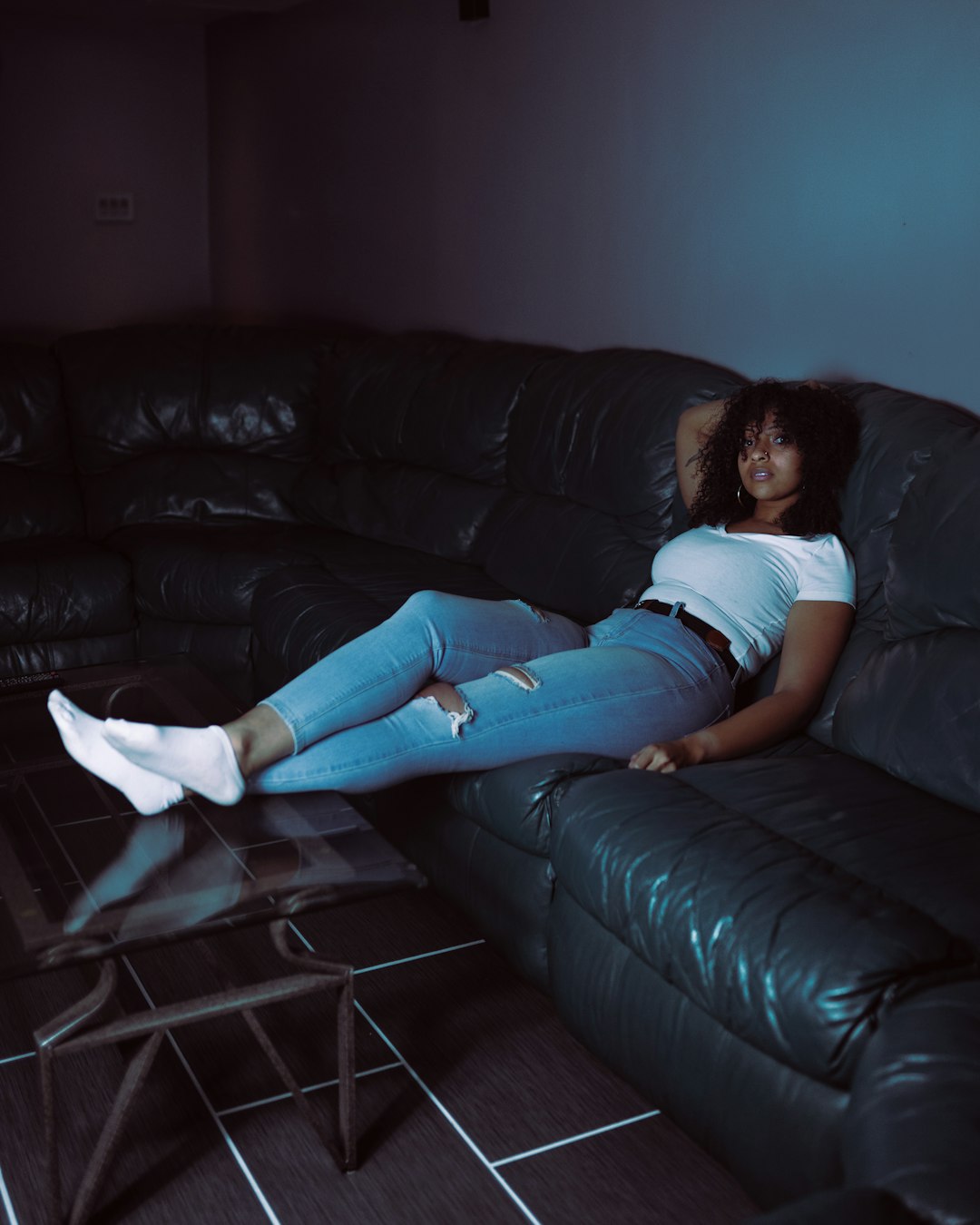 woman in white t-shirt and blue denim jeans lying on black leather couch