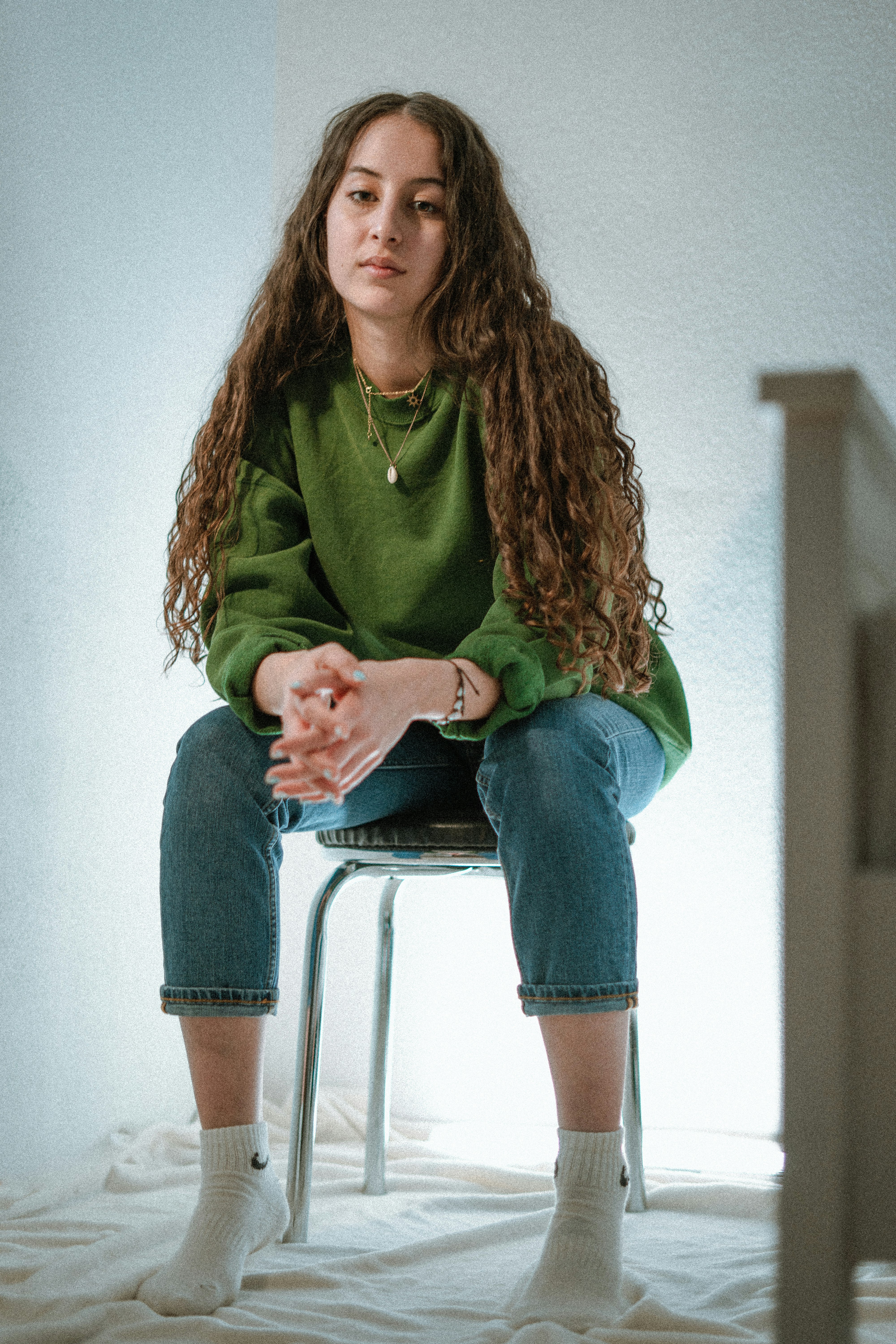 woman in green long sleeve shirt and blue denim jeans sitting on white chair