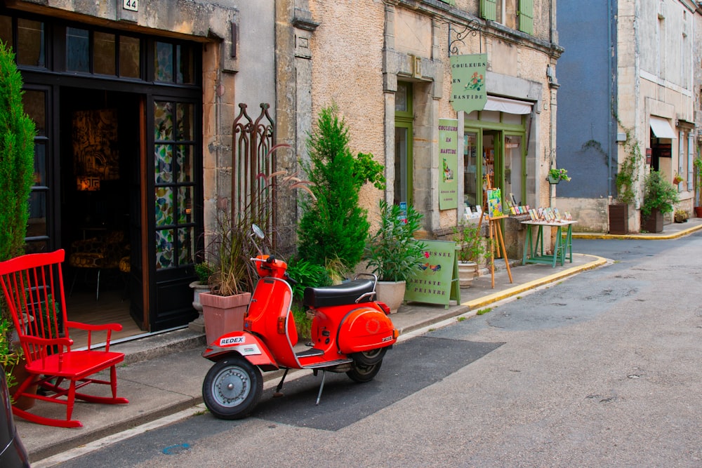 red and black motor scooter parked beside brown concrete building during daytime