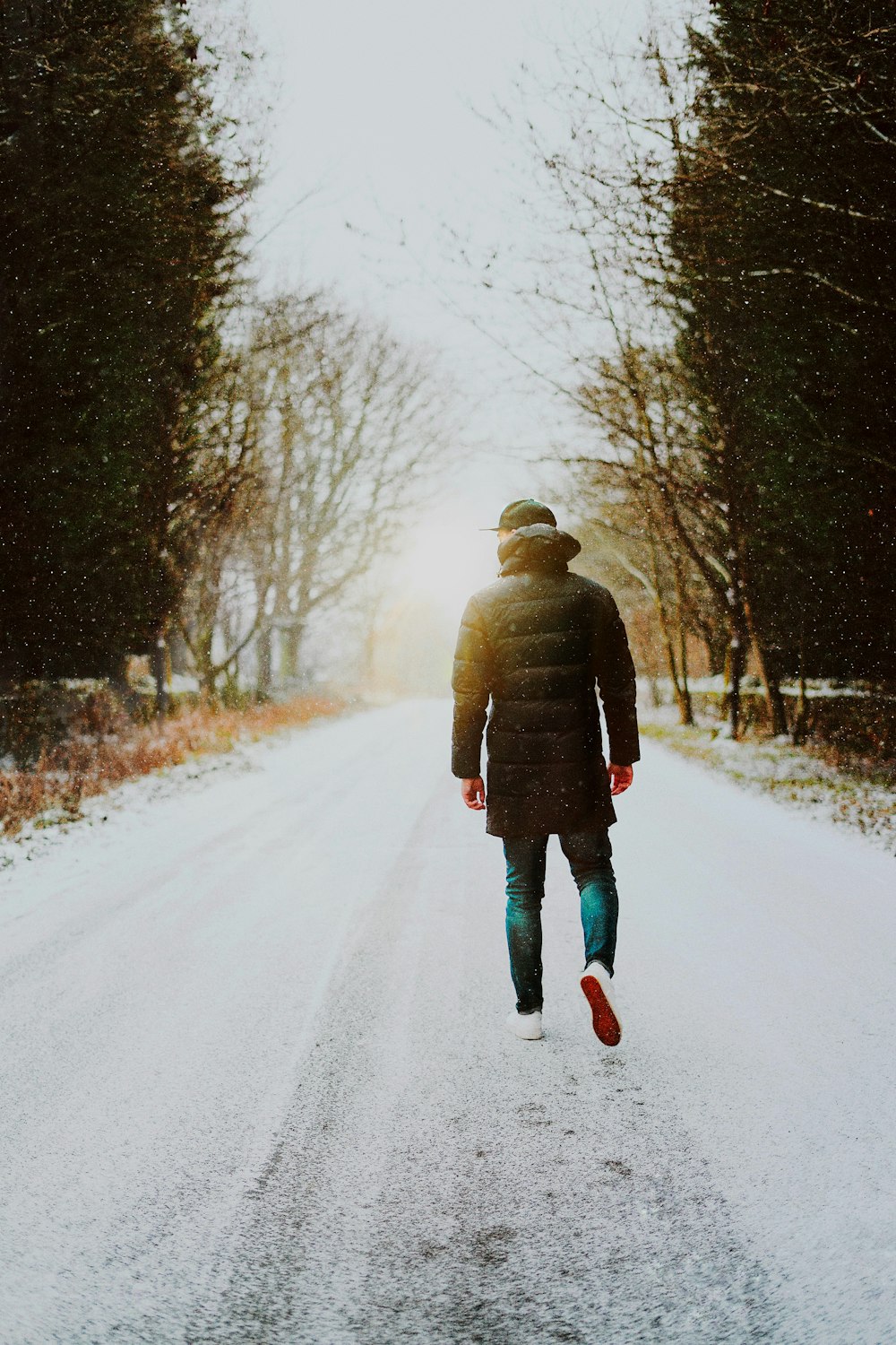 person in brown jacket walking on snow covered road during daytime